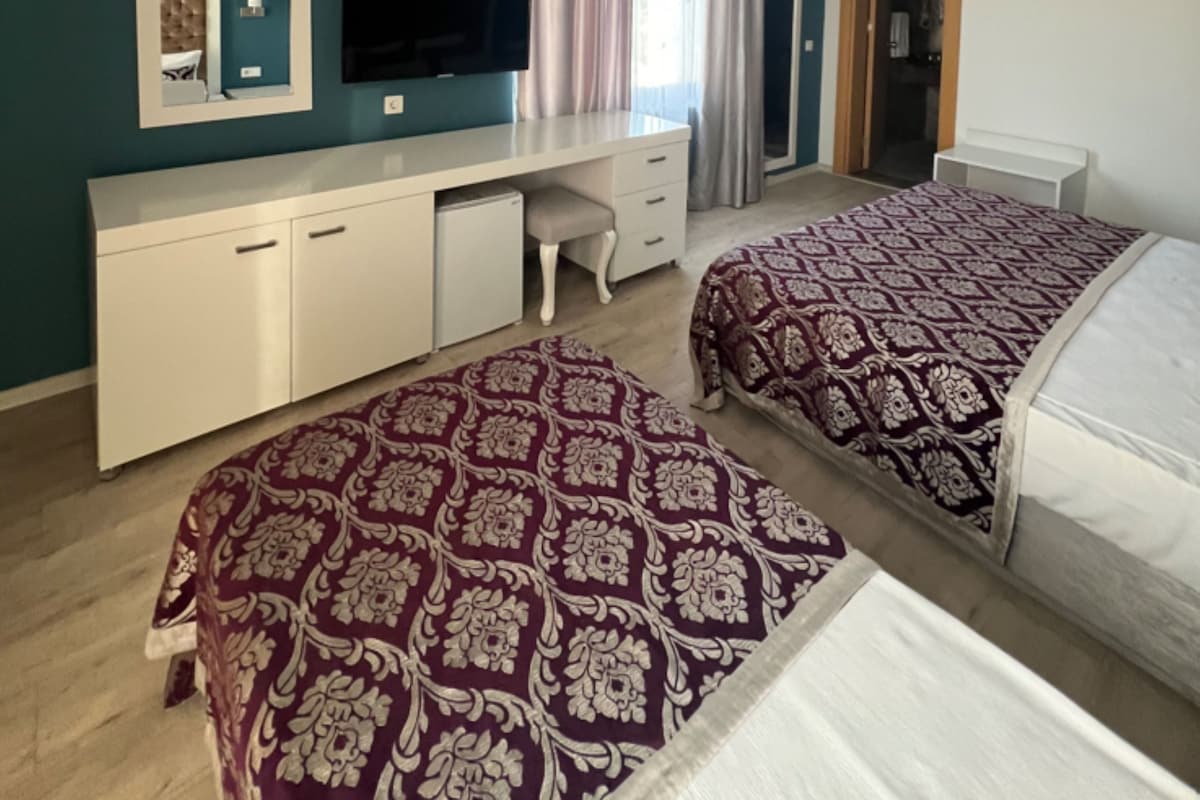 Una habitación de hotel con escritorio, dos camas, televisor y ventana con cortinas.
