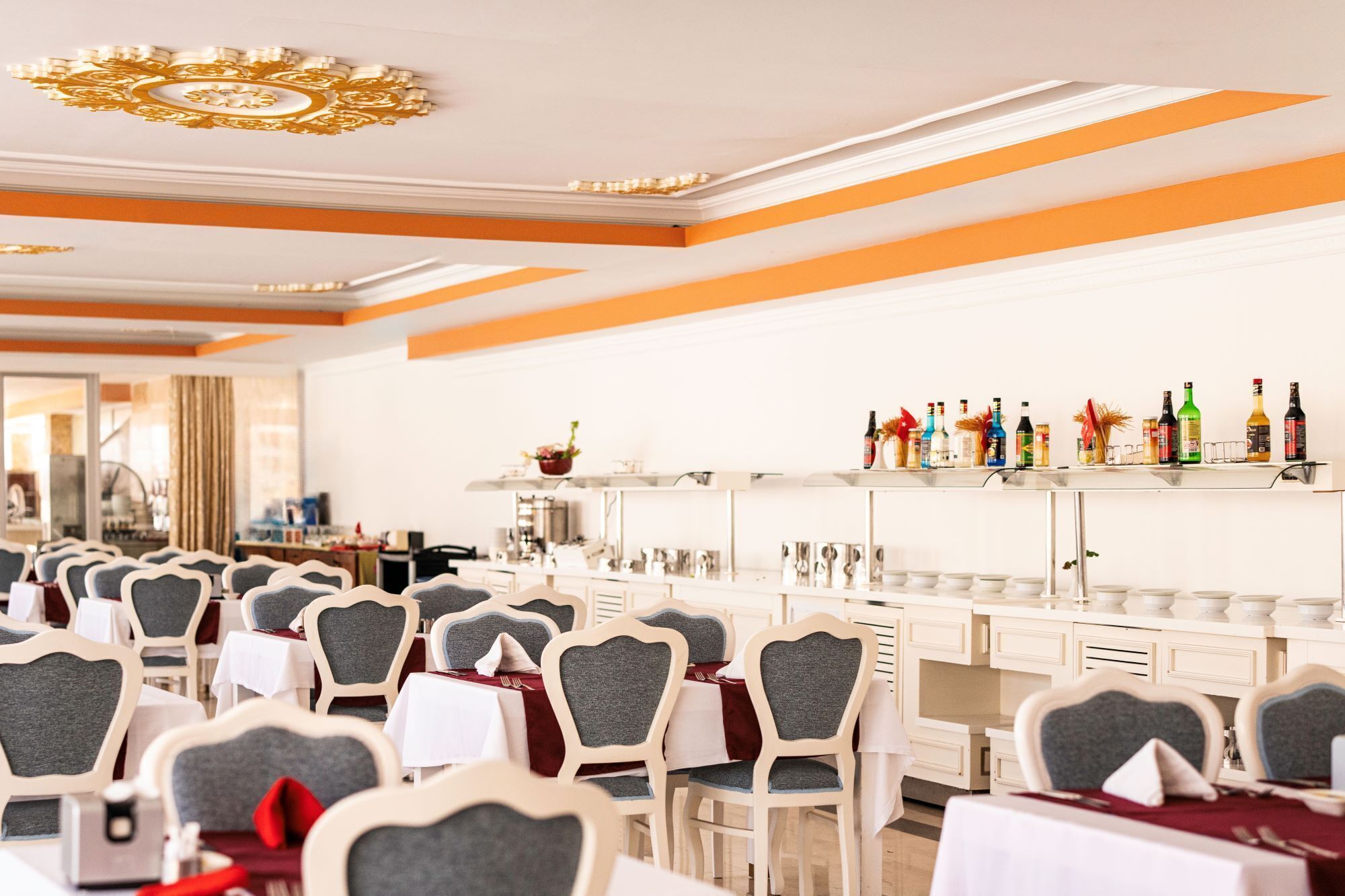 Un restaurante con decoración blanca y naranja, varias mesas y una zona de bar con diferentes botellas.