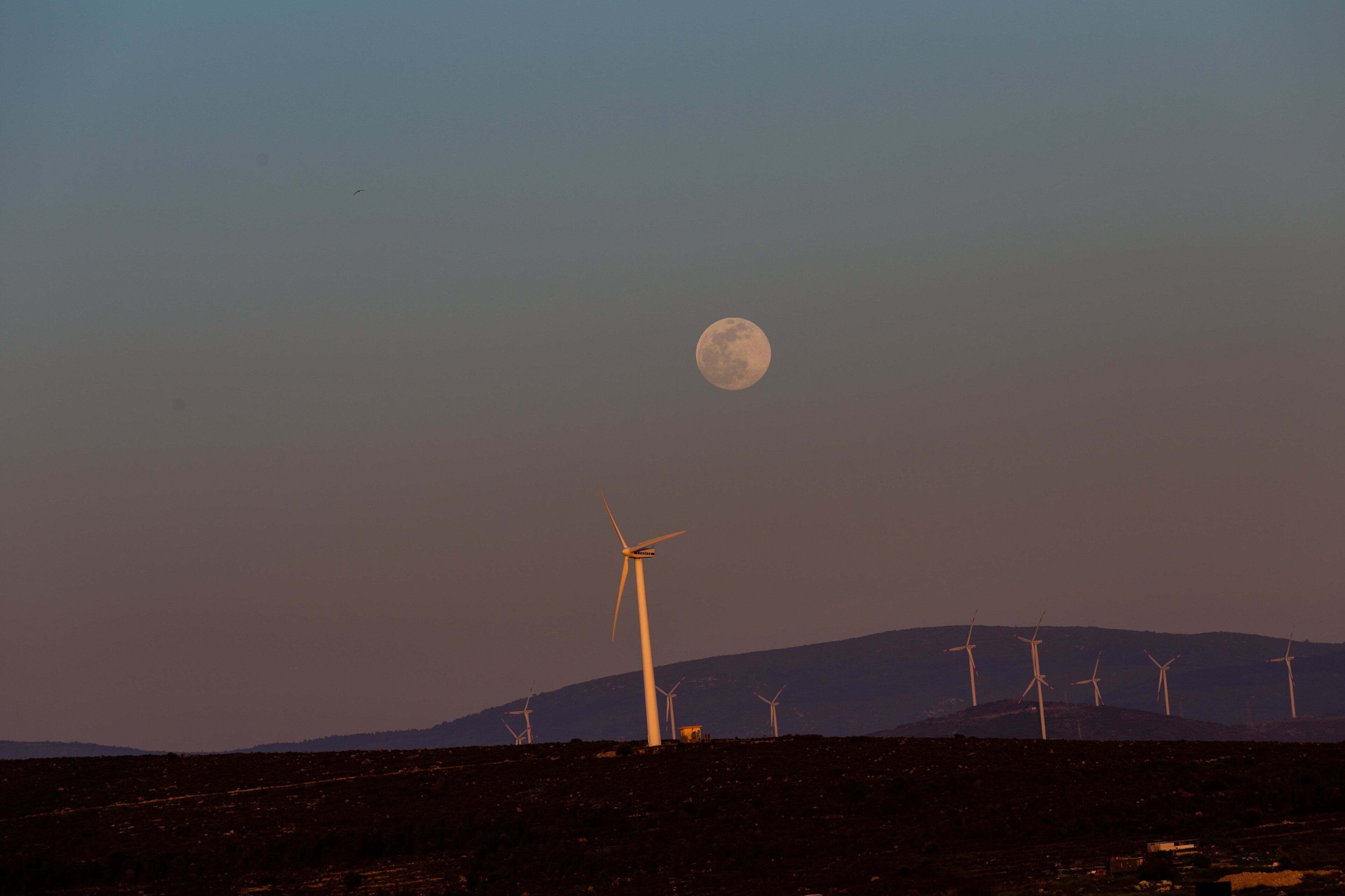 A landscape with wind turbines and a full moon in the sky.