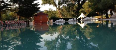 A swimming pool with lounge chairs, a small red building, and a white tent.
