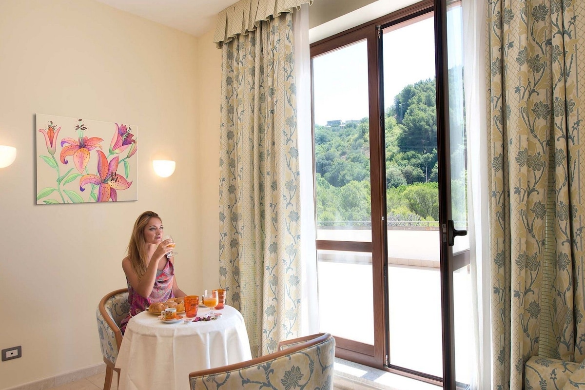 Un coin repas avec une table mise pour le petit-déjeuner, un tableau accroché au mur et une vue sur la verdure, visible à travers une porte coulissante.
