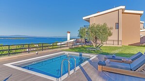 A swimming pool with a view of the sea, a modern building, and a small tower. - Sea View Villas (Sithonia)