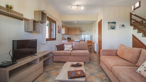 A modern living room with a flat-screen TV, a sofa, a coffee table, and a kitchen in the background. - Sea View Villas (Sithonia)