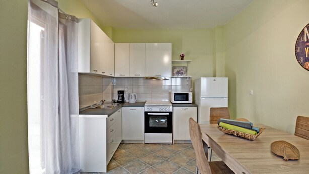 A compact kitchen with a stove, microwave, and refrigerator. There is a dining table with chairs and a basket of items on it. - Sea View Villas (Sithonia)