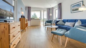 Ein modernes Wohnzimmer mit einem blauen Sofa, Holzmöbeln und Blick auf einen Leuchtturm durch große Fenster.