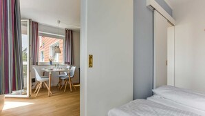 Ein Hotelzimmer mit einem Bett, einer Essecke mit Stühlen und Tisch sowie Blick auf das äußere Gebäude.