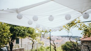 Un dosel blanco con luces esféricas colgantes, una pared de piedra y follaje en el fondo.