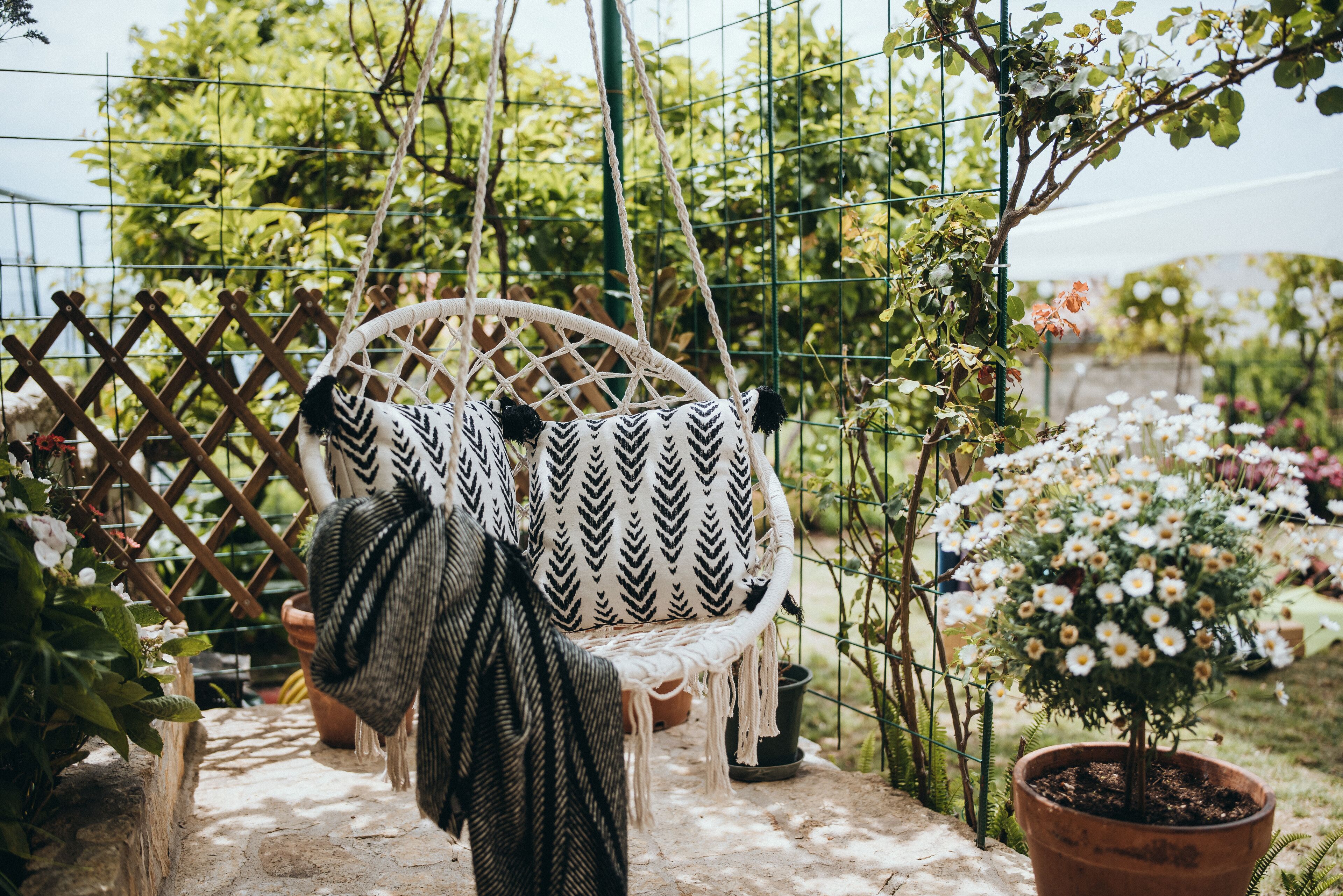 A wicker chair with a black and white chevron pattern, positioned in a garden with a lattice fence and potted plants.