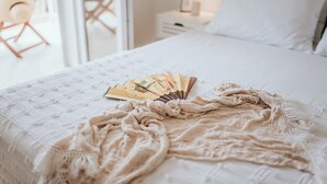 Una cama con un edredón blanco, una manta color beige y un ventilador.
