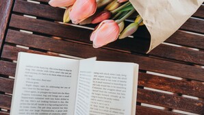 Un libro abierto sobre una superficie de madera, con un ramo de tulipanes rosados al fondo.