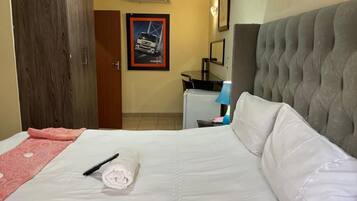 A hotel room with a bed, a desk, a chair, and a door.