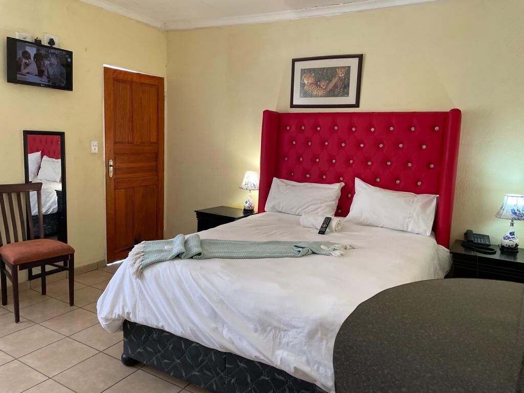 Een hotelkamer met een rode, gestoffeerde hoofdeinde, een bed met witte lakens, een stoel, een houten deur en een televisie aan de muur.
