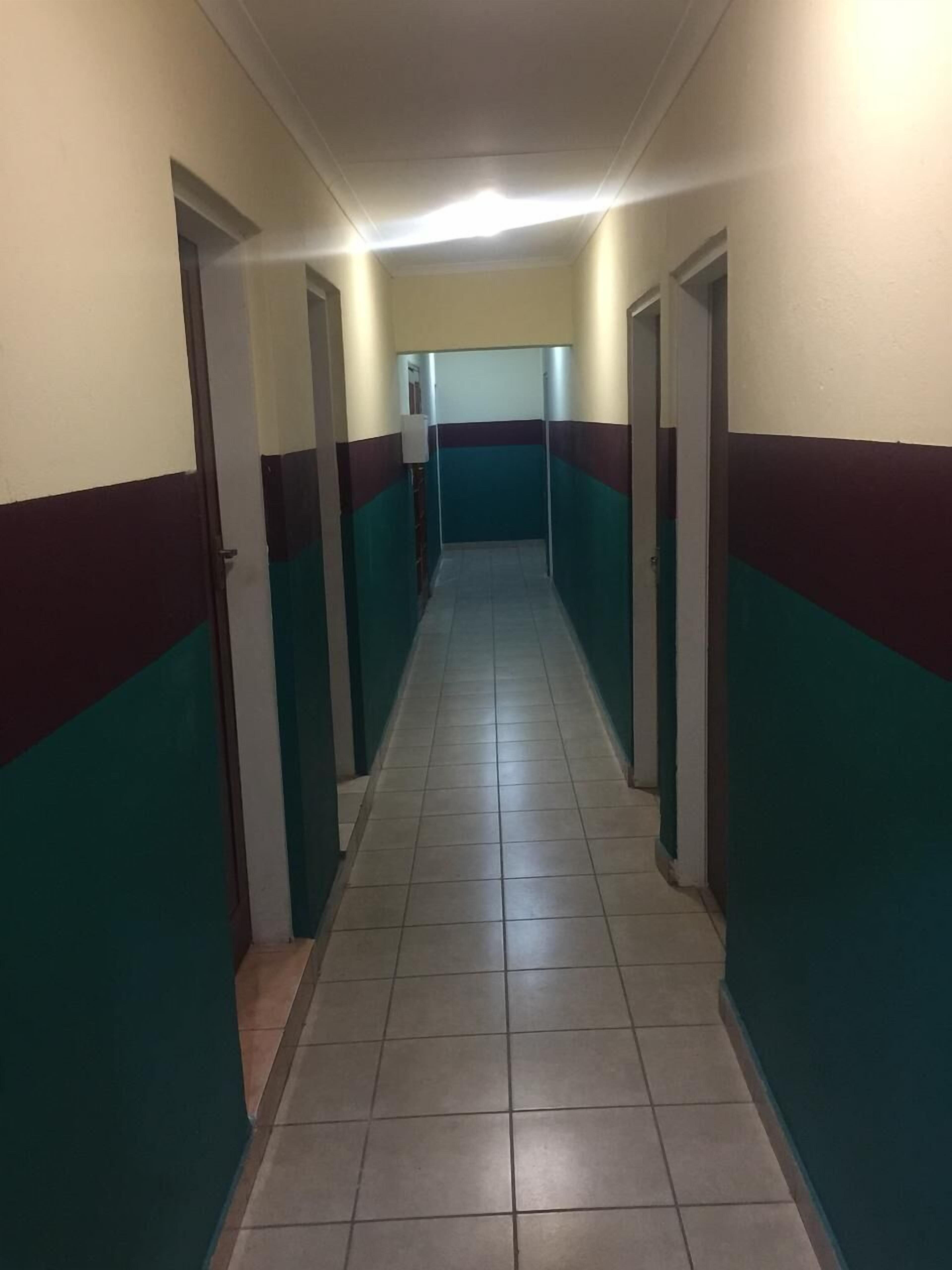 Un long couloir étroit, doté d’un sol carrelé et de murs peints de bandes alternées de couleurs turquoise et bordeaux.