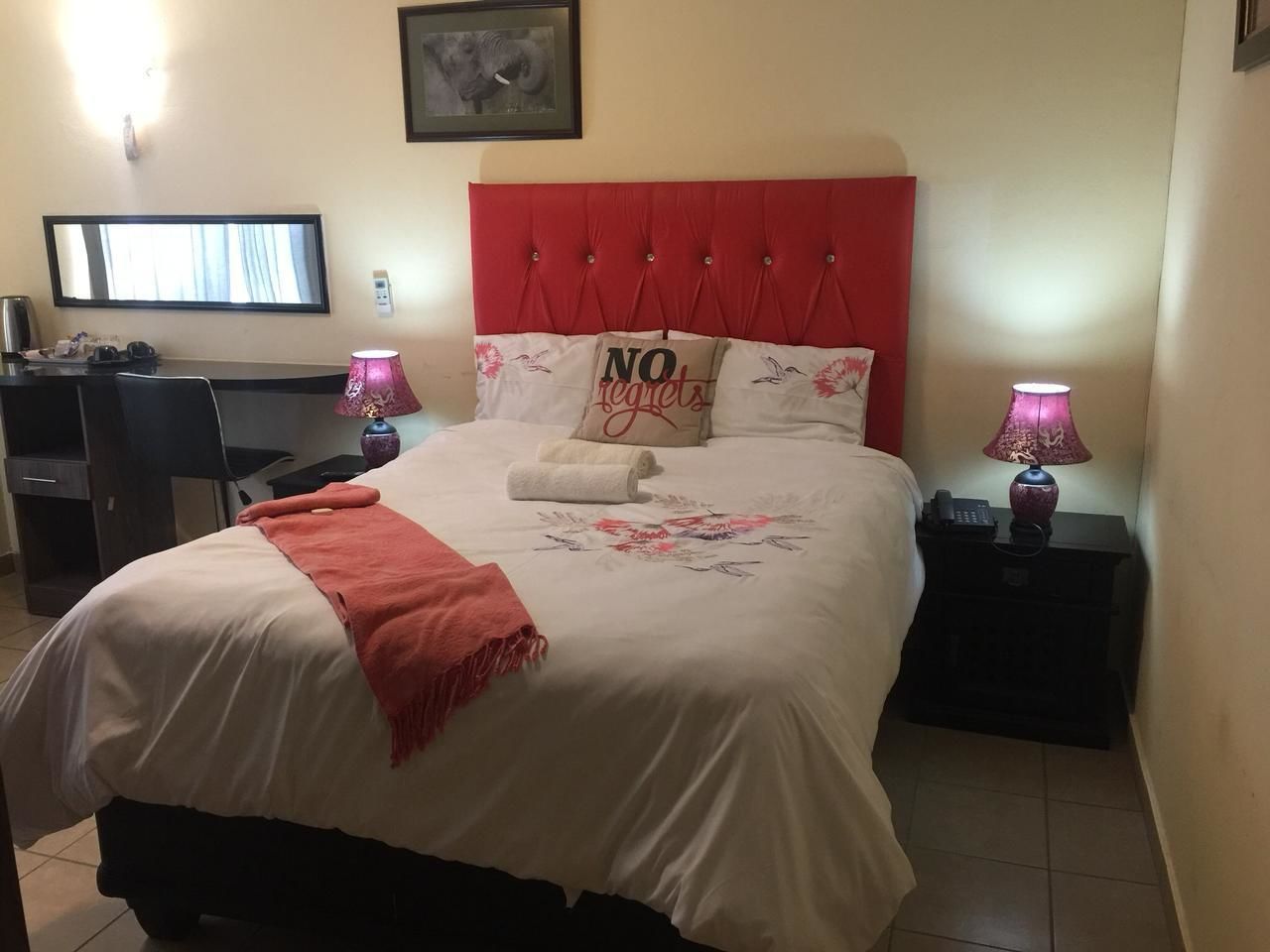 A hotel room with a bed, a desk, a chair, two bedside lamps, and a framed picture on the wall.
