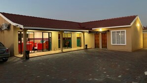 A building with a tiled roof, a covered patio area with red chairs, and a car parked in front.