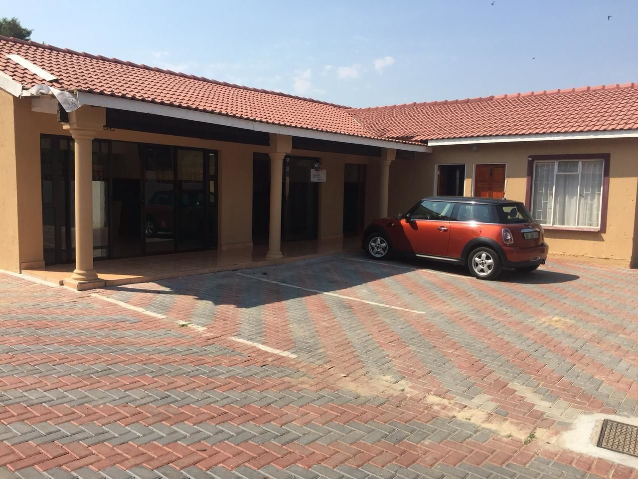 A building with a red-tiled roof, a red car parked in front, and a paved entrance area.