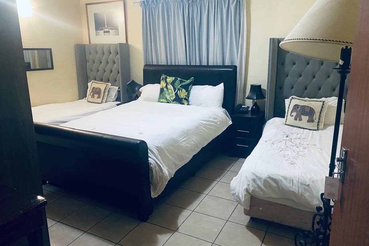 Une chambre d’hôtel avec deux lits, une table de chevet, une lampe et une fenêtre avec des rideaux.