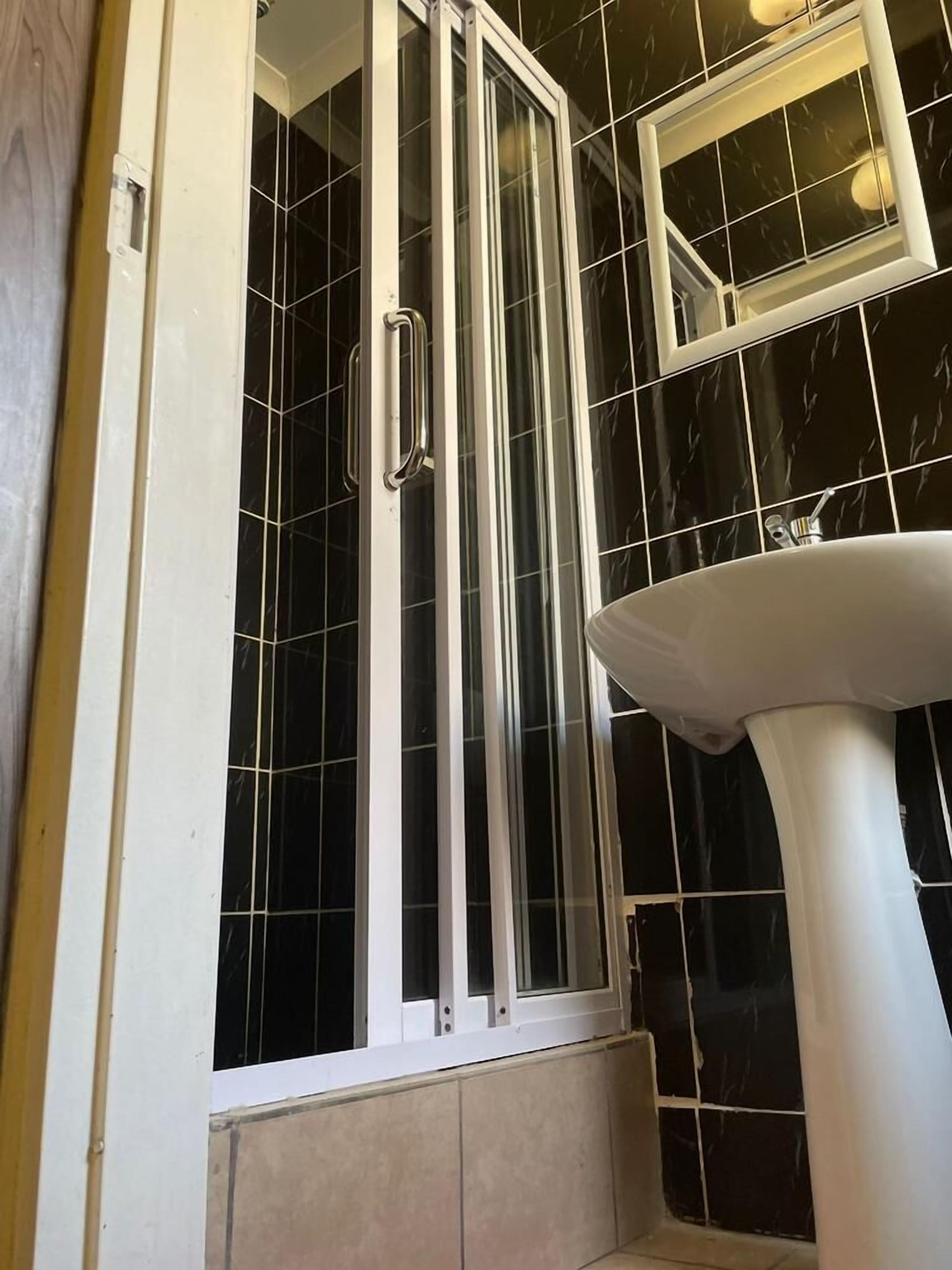 Un bagno con doccia vetrata, un lavandino bianco e piastrelle in marmo nero.