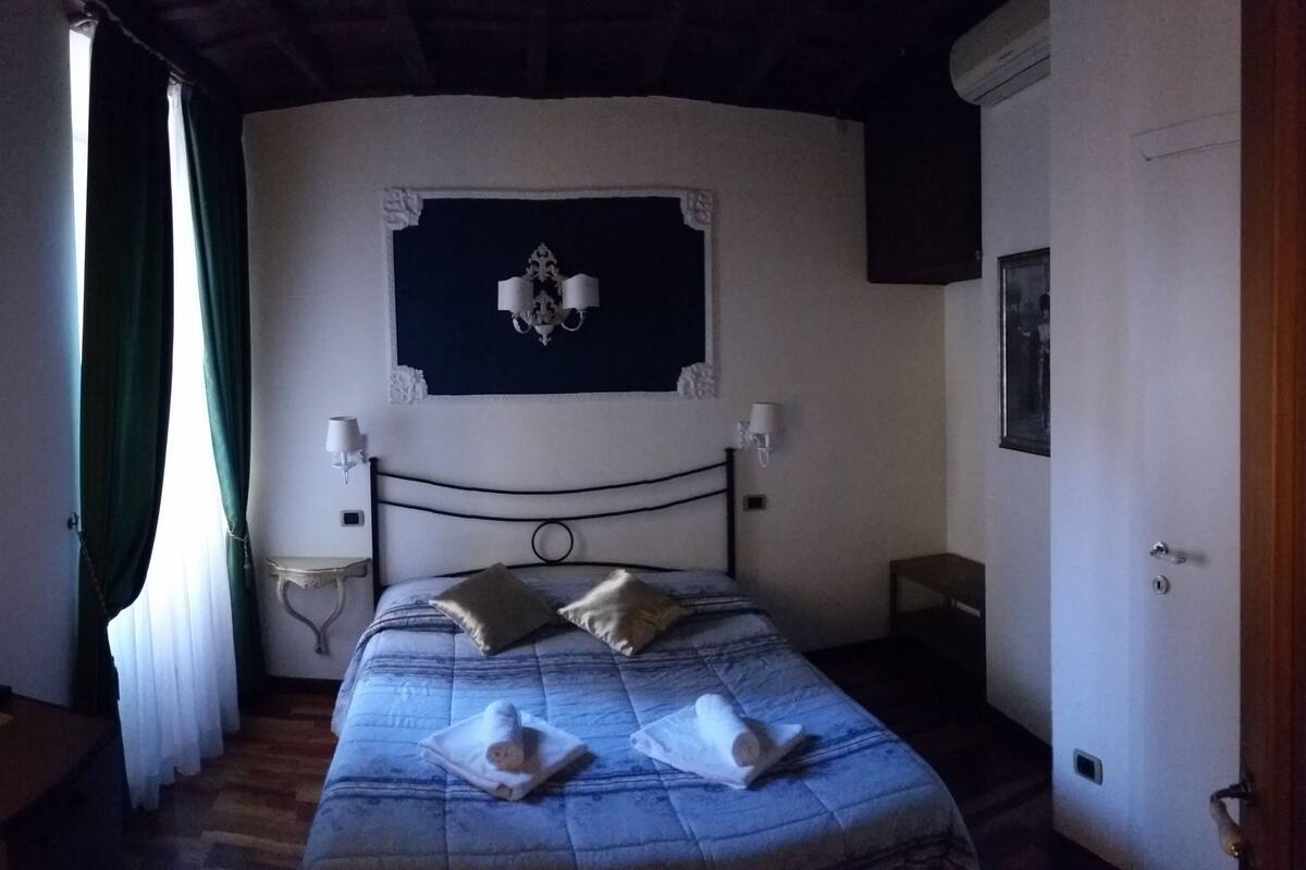 A bedroom with a bed, a bedside table, a mirror, and a wall-mounted lamp.