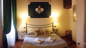 A neatly made bed with a patterned bedspread, two bedside lamps, and a wall-mounted light fixture. - Diapason Colosseum Suite (Rome)