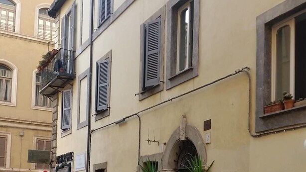 A cobblestone street with a parked motorcycle, a dog walking, and a person riding a scooter. - Diapason Colosseum Suite (Rome)