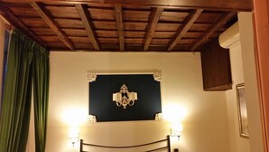 A room with a wooden ceiling, a black accent wall, a chandelier, and two wall-mounted lamps. - Diapason Colosseum Suite (Rome)
