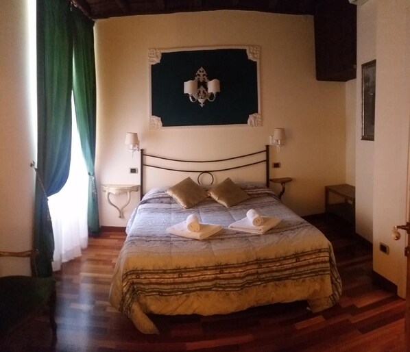 A neatly made bed with a striped bedspread and two pillows, a wall-mounted light fixture, and a small bedside table with a lamp.