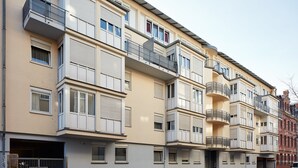 A multi-story residential building with balconies, a gated entrance, and parked cars. - Apartments 4 YOU - Lange Strasse (Fuerth)