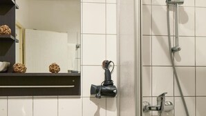 A bathroom with a white tiled wall, a glass shower enclosure, a mirror, and a sink with a soap dispenser. - Apartments 4 YOU - Lange Strasse (Fuerth)