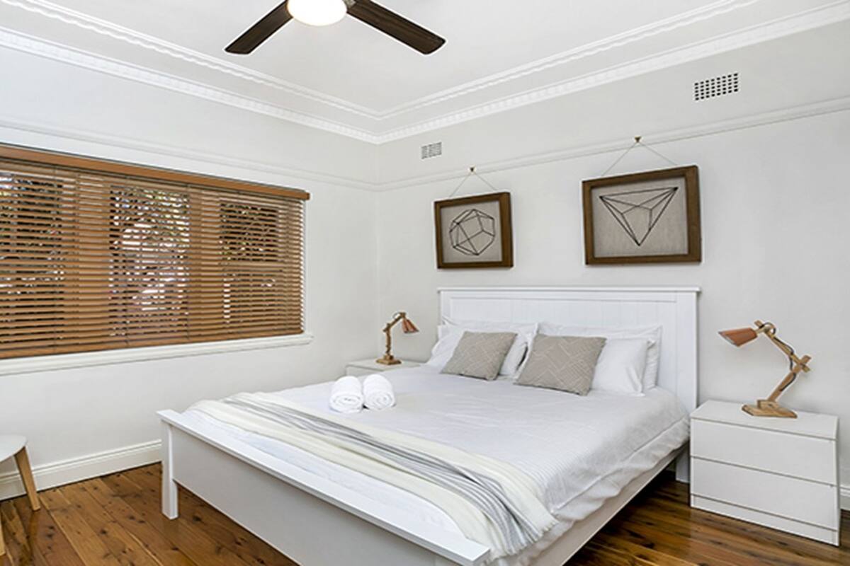 A bedroom with a large bed, two bedside tables, a chair, and a ceiling fan.