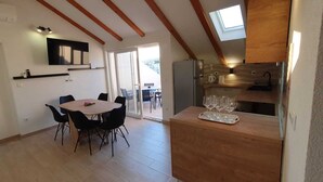 A dining area with a round table and chairs, a kitchen with a countertop and wine glasses, and a view through a glass door to an outdoor balcony. - Apartments and Rooms Zvjezdana (Hvar)
