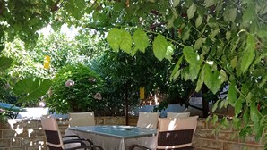 An outdoor patio with a table and chairs, surrounded by greenery and a stone wall. - Apartments and Rooms Zvjezdana (Hvar)