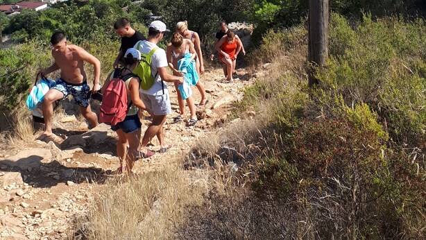 A group of people hiking on a rocky path with a coastal view in the background. - Apartments and Rooms Zvjezdana (Hvar)