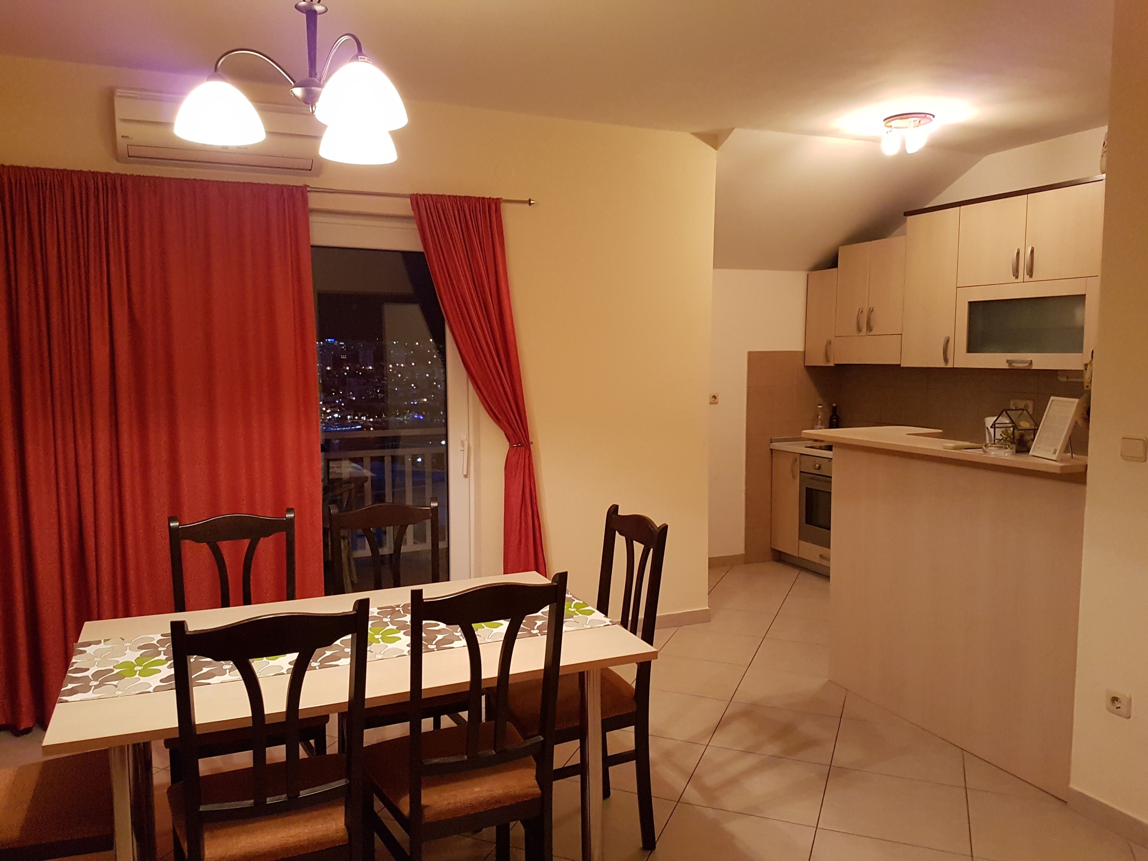 A dining area with a table and chairs, a kitchen with cabinets and appliances, and a view of the city at night through a window.
