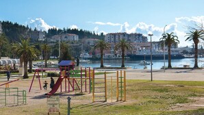 A playground with slides and climbing structures, a body of water, and buildings in the background. - Cozy apartment in Ploce with WiFi (Ploce)