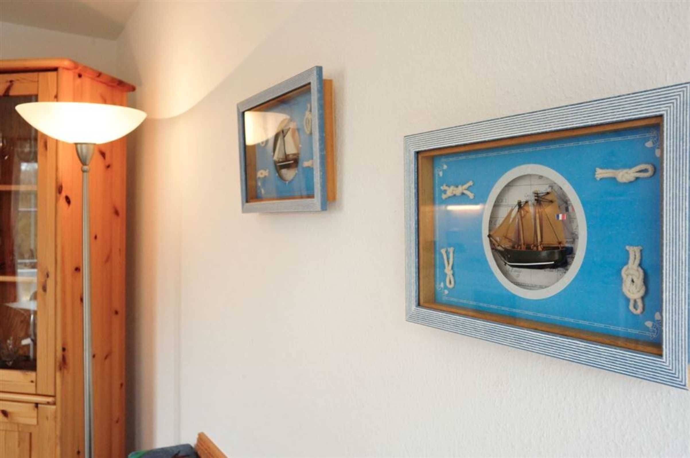 En inramad tavla med marint tema på väggen, ett träskåp och en lampa.