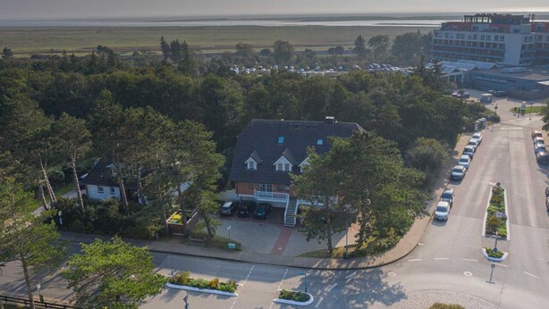 A hotel with a central building surrounded by trees, a parking lot, and a view of the sea. - Apartment 8 Strandstar (ID 118) (Sankt Peter-Ording)