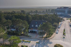 A hotel with a central building surrounded by trees, a parking lot, and a view of the sea.