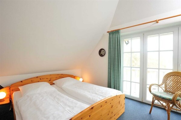 A bedroom with a wooden bed, a chair, and a window with curtains.