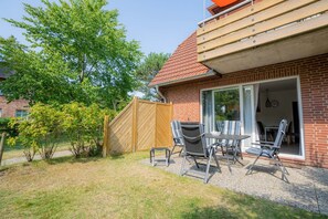 Une terrasse avec une table et des chaises, une clôture en bois et une maison en briques avec un toit rouge.