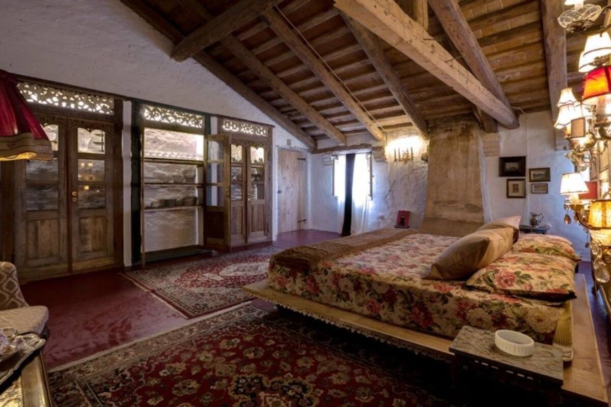 A bedroom with a large bed, wooden beams, a red carpet, and a chandelier.