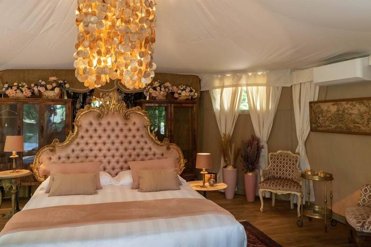 A luxurious bedroom with a tufted headboard, a chandelier, and classic decor.