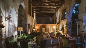 Un interior rústico con poca luz, que incluye un comedor, muebles antiguos y una pared de piedra.
