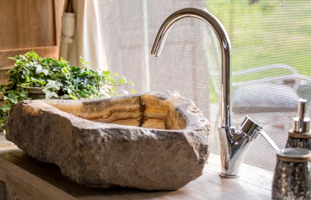 A stone basin sink with a modern faucet, surrounded by greenery and a window with a view.