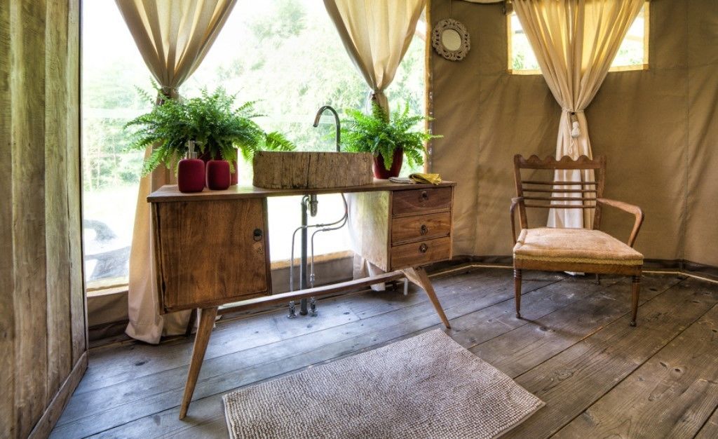 A rustic wooden desk with a sink, two potted plants, and a chair in a room with wooden flooring and beige curtains.