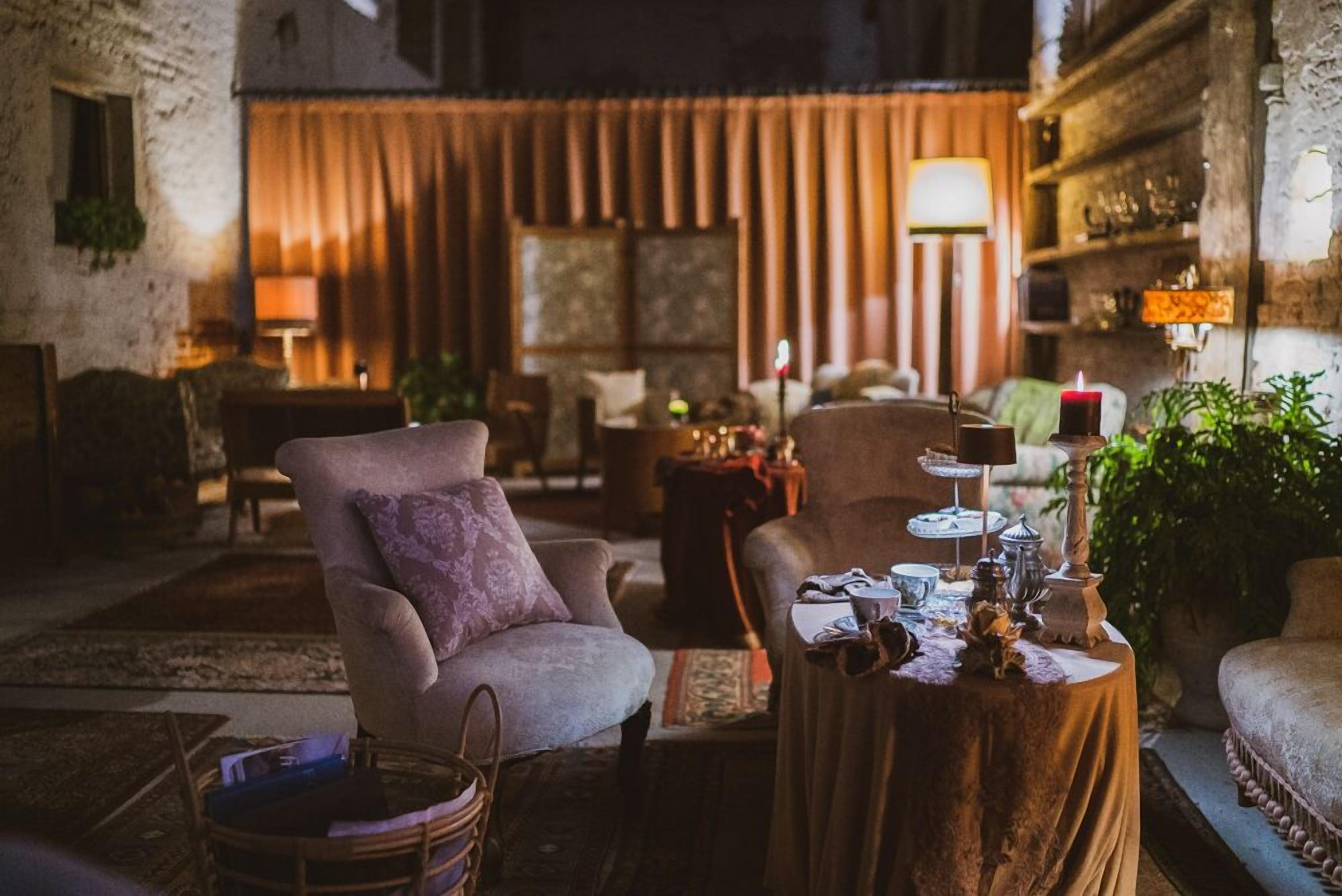A cozy, dimly lit room with vintage furniture, including a plush armchair and a small round table with a candle and decorative items.