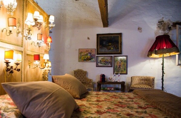 Une chambre confortable avec un lit, deux fauteuils, une table sur laquelle sont posés divers objets et des lampes fixées au mur.