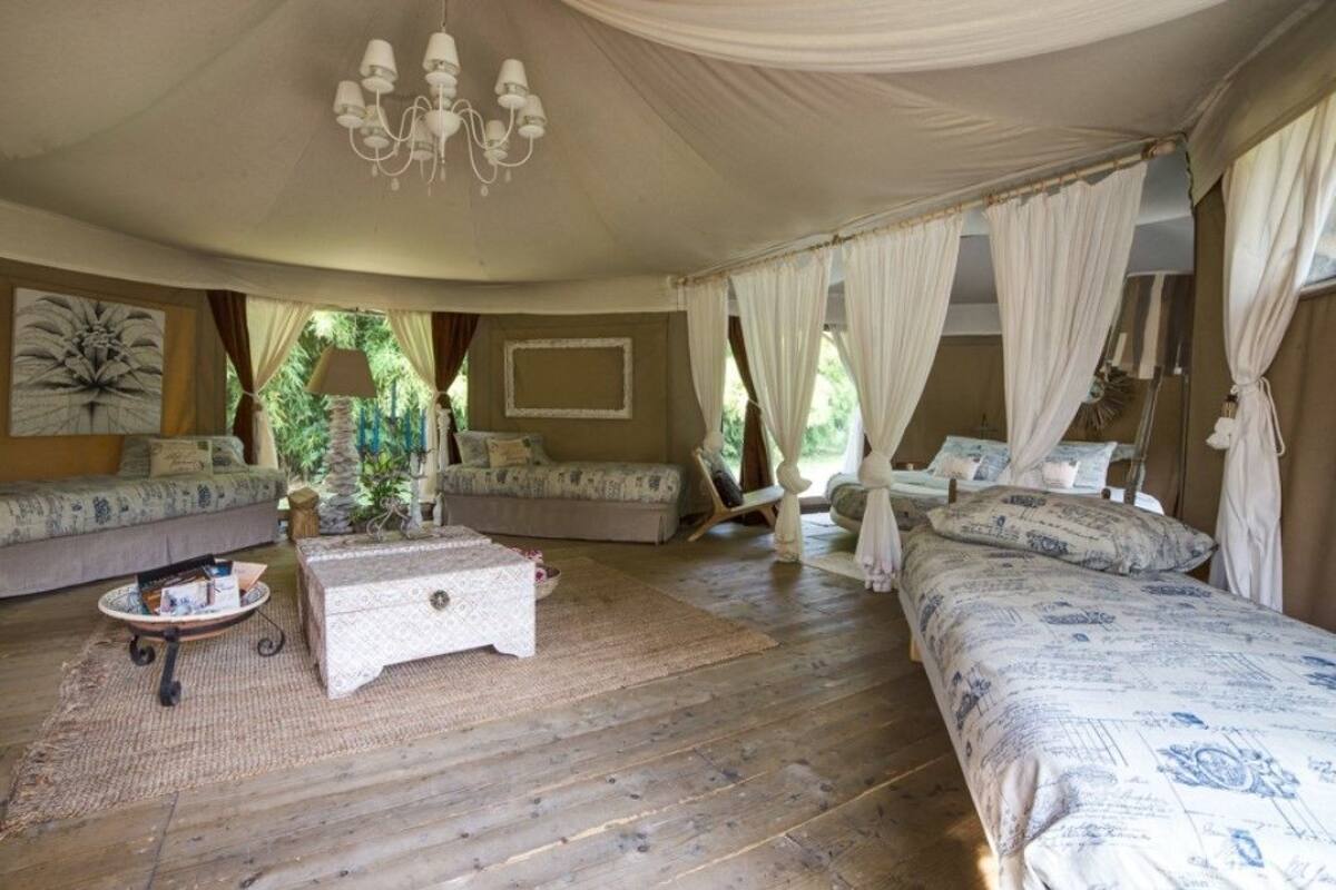 A tent-style bedroom with two beds, a sofa, a small table, and a chandelier.