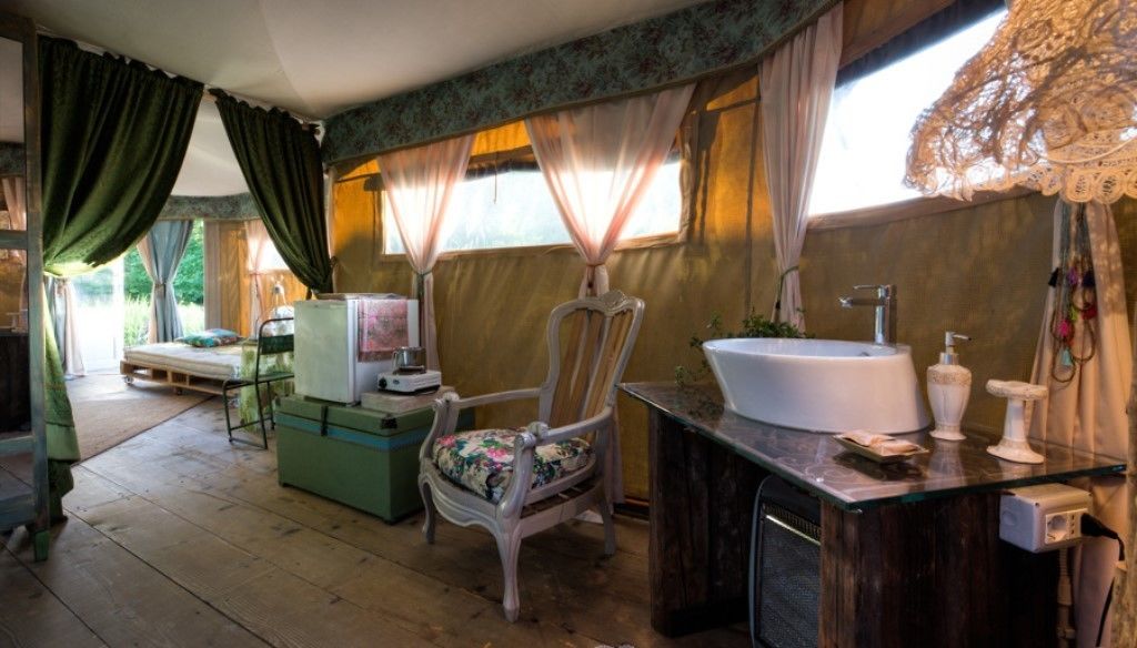 A room with a bed, a chair, a desk, a sink, and a window with curtains.