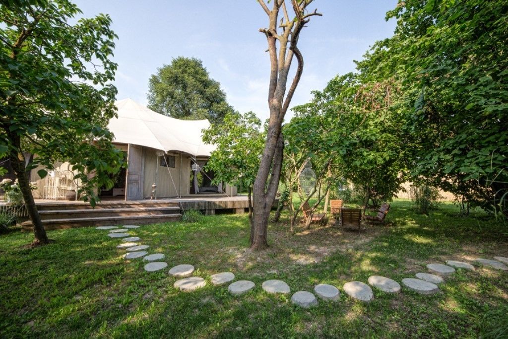 Un jardín con terraza de madera, un árbol y un edificio de techo blanco.
